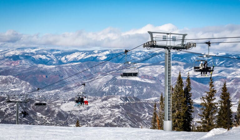 Skiers and snowboarders ascend the Elk Camp chairlift at the Aspen Snowmass ski resort, in the Rocky Mountains of Colorado on a partly cloudy winter day.