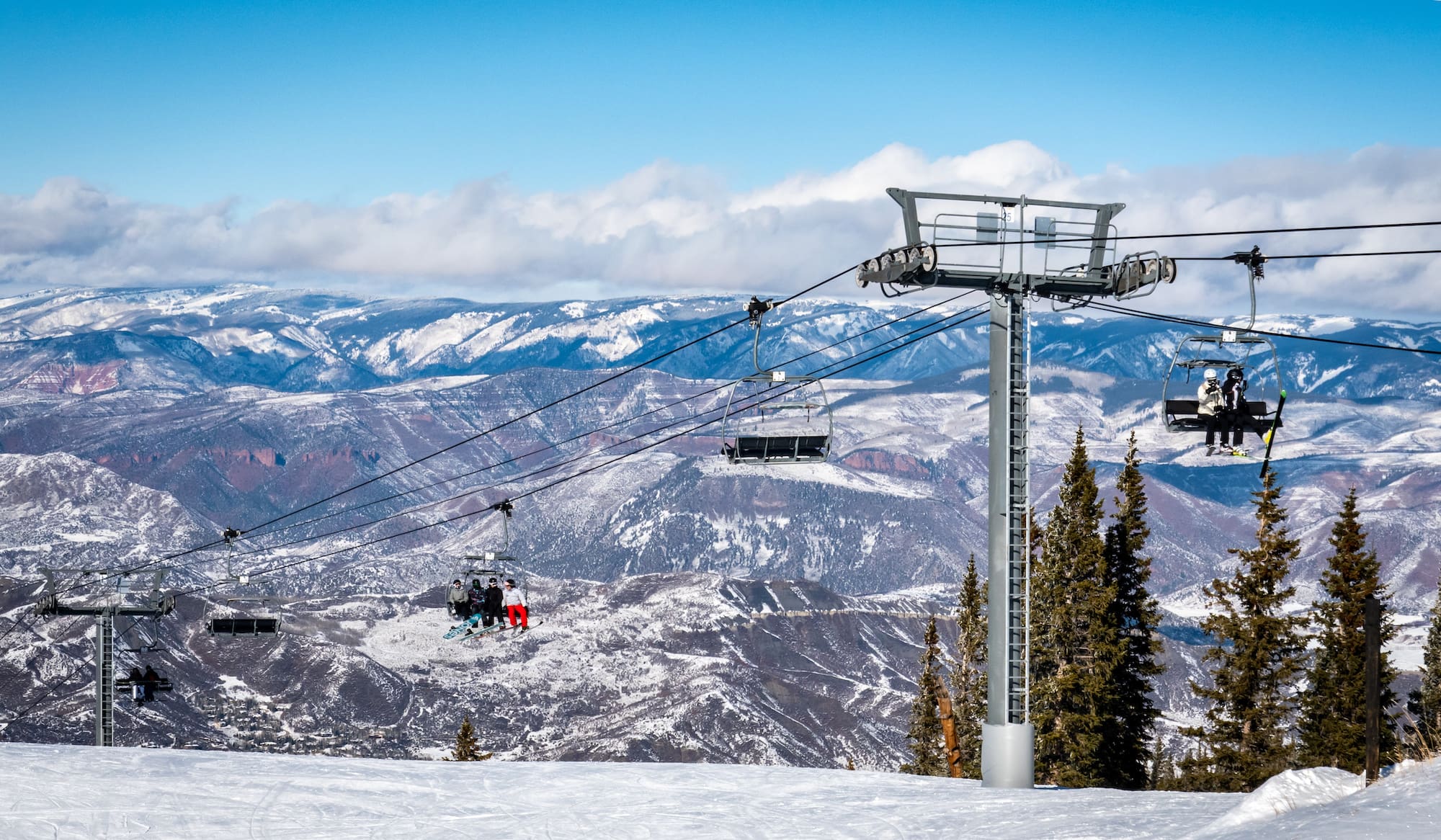 Skiers and snowboarders ascend the Elk Camp chairlift at the Aspen Snowmass ski resort, in the Rocky Mountains of Colorado on a partly cloudy winter day.
