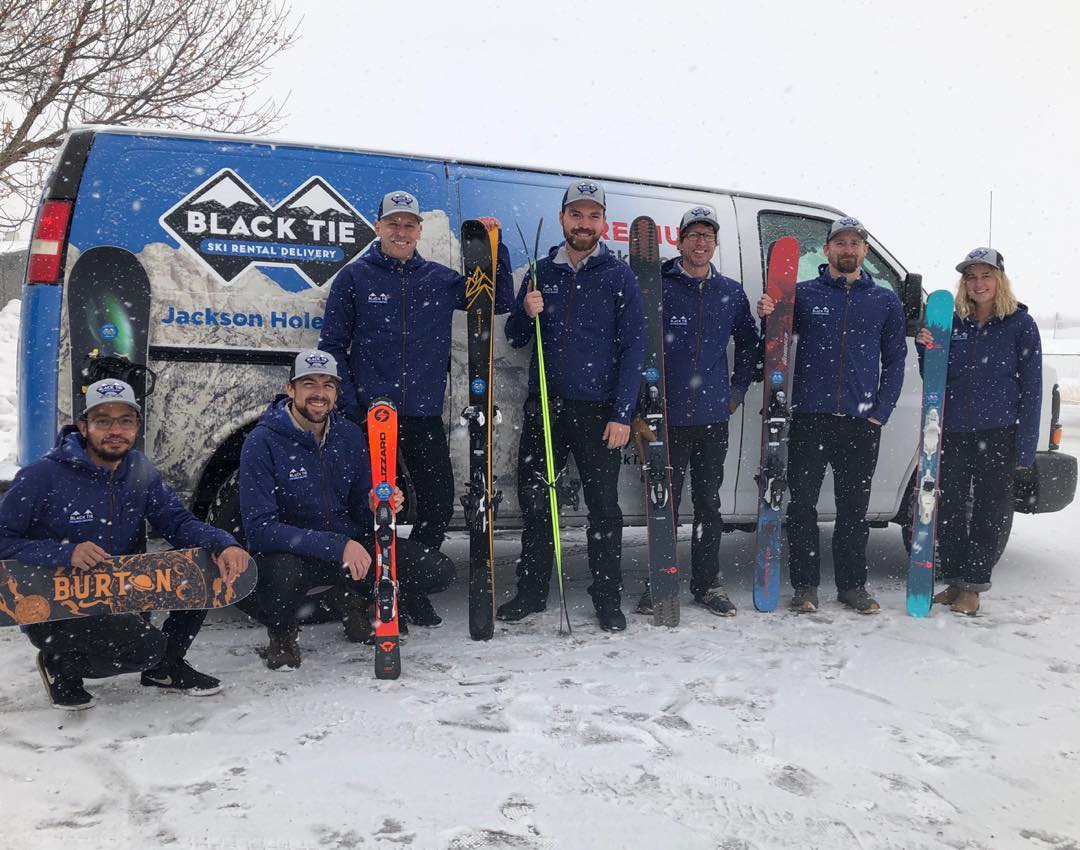 black tie ski rental technicians with rental gear standing next to delivery van