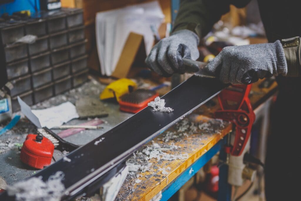A male worker in a ski service workshop repairs the sliding surface of the skis. Close-up of a hand with a plastic scrapper for removing wax, removing new wax. 