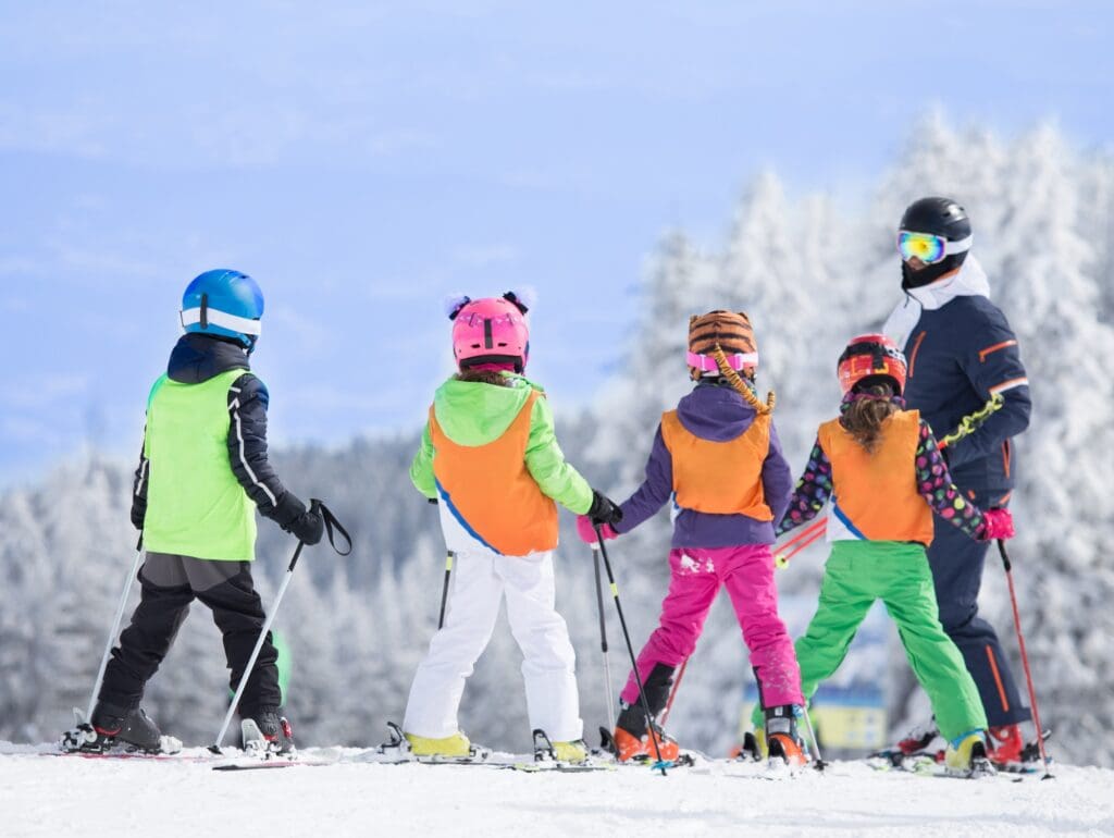 Group of kids learning how to ski on slope with instructor. Blue sky and white firs in background