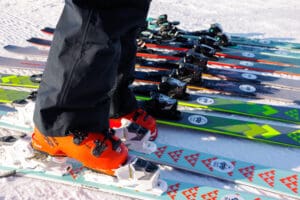 a person in orange ski boots and black ski pants tries on a new pair of skis